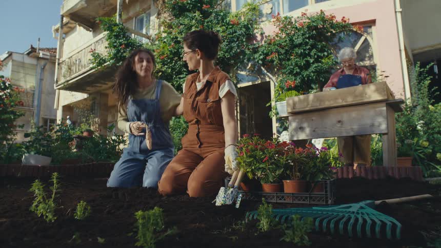A loving mother and daughter plant seedlings together in their garden, while the grandmother works nearby, creating a heartwarming multi-generational family scene