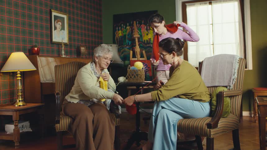 A grandmother, mother, and daughter share a peaceful moment knitting together at home