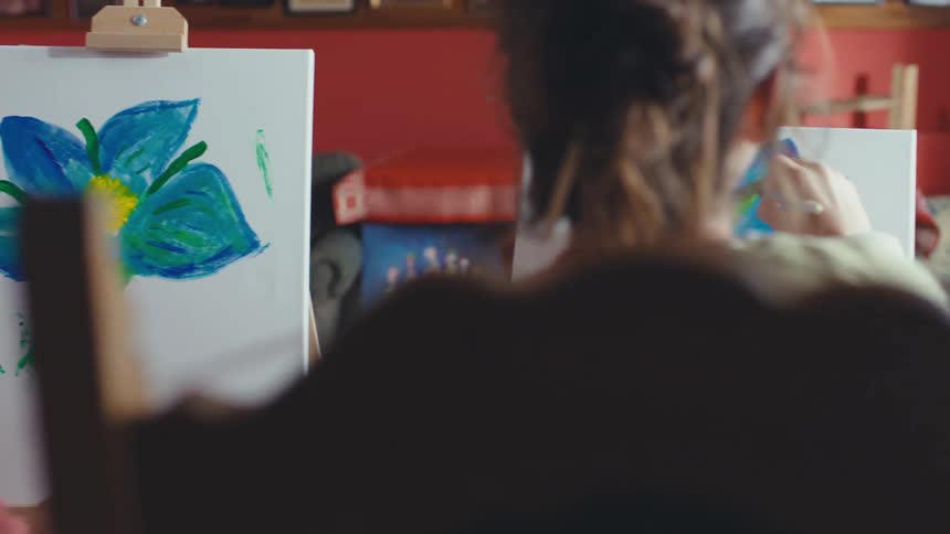 Over-the-shoulder slow-motion pan of a multi-generational art class painting flowers and ballerinas