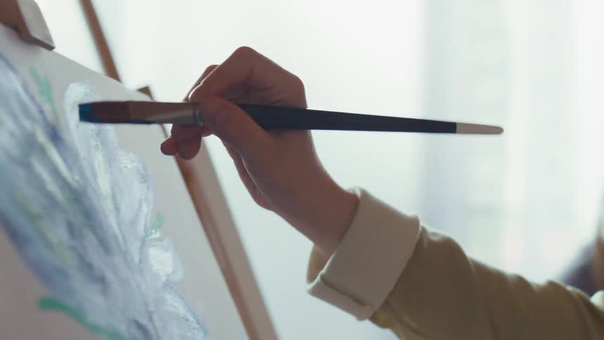 A young artist focuses intently as she applies a stroke of blue paint to her abstract floral canvas during a peaceful art class