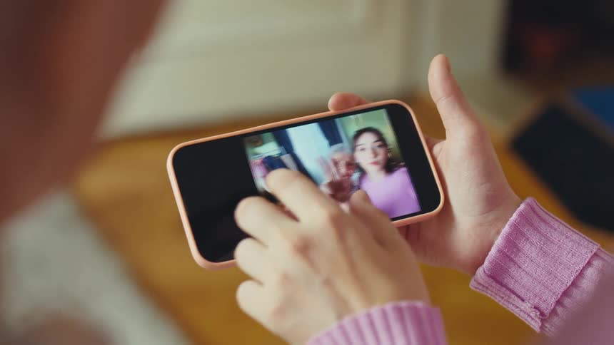 An over-the-shoulder view of hands scrolling through a heartwarming selfie video of a grandmother and granddaughter on a smartphone