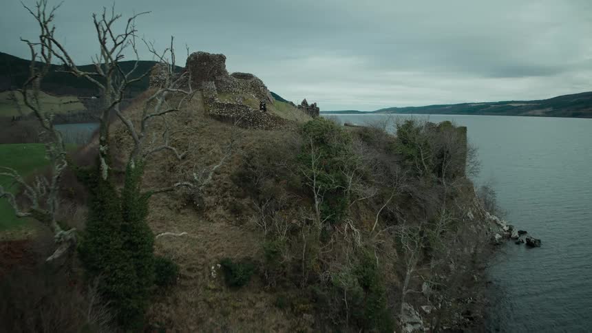 Aerial view reveals a Scottish bagpiper in a kilt playing within the historic ruins of Urquhart Castle on the shores of Loch Ness