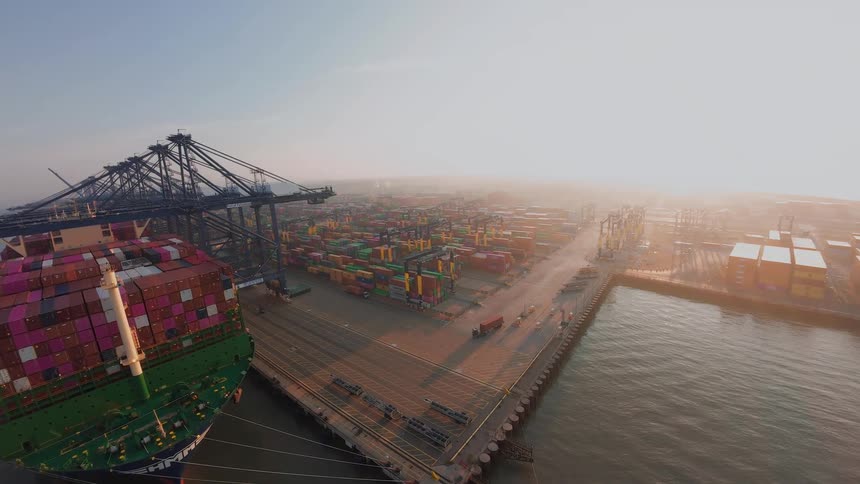 A breathtaking high-angle aerial view of a huge container ship docked at a sprawling port during a hazy golden sunrise