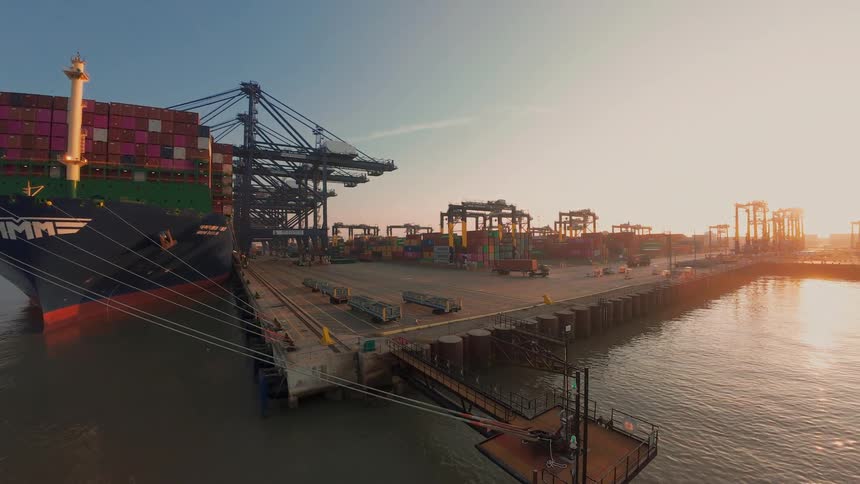 A majestic sunrise timelapse shows a busy shipping port with a large container vessel docked for loading