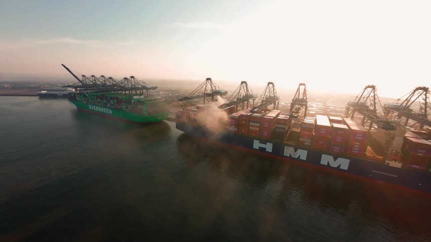 A stunning aerial shot captures massive container ships being loaded by cranes at an industrial port during a hazy sunrise