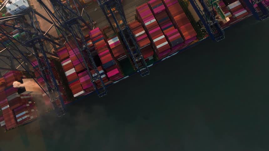Aerial top-down view of a massive container ship being loaded by cranes at a busy industrial port