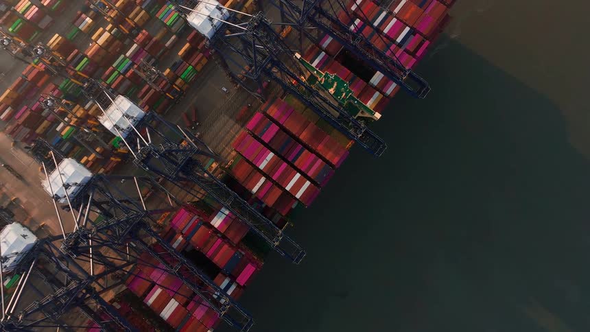 A static aerial top-down view of large cranes loading and unloading colorful shipping containers at a busy industrial port