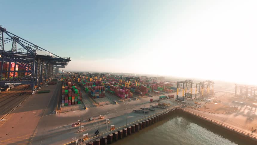 A timelapse of a bustling shipping port at sunrise, with cranes loading and unloading colorful containers as trucks move throughout the yard