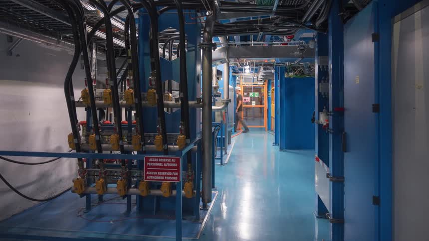 Dolly forward through a high-tech industrial service corridor where engineers and technicians are conducting work and inspections