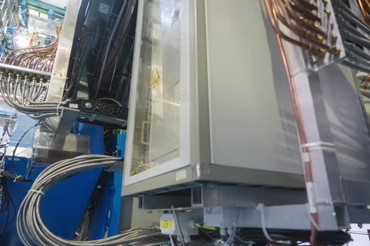 A low-angle tracking shot reveals the immense scale and complex electronic components of the ATLAS particle detector at CERN