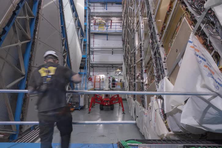 Timelapse dolly shot reveals the vast interior of a particle accelerator facility with engineers working on the equipment