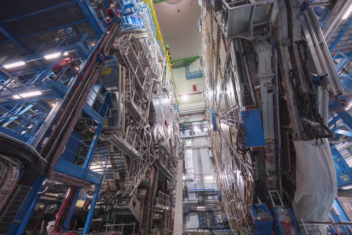 A time-lapse shows engineers and technicians assembling a massive, complex particle detector in a high-tech scientific research facility