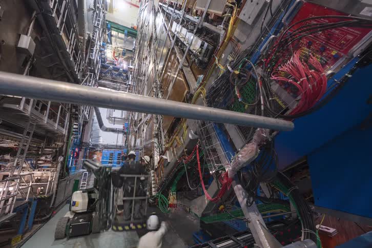 A dynamic timelapse captures engineers performing maintenance on the intricate wiring and components of a massive particle detector deep underground