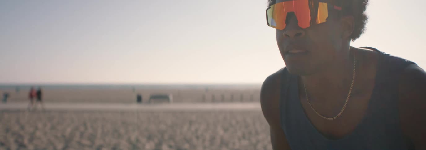 A focused young man wearing reflective sunglasses concentrates intently on the beach in slow motion