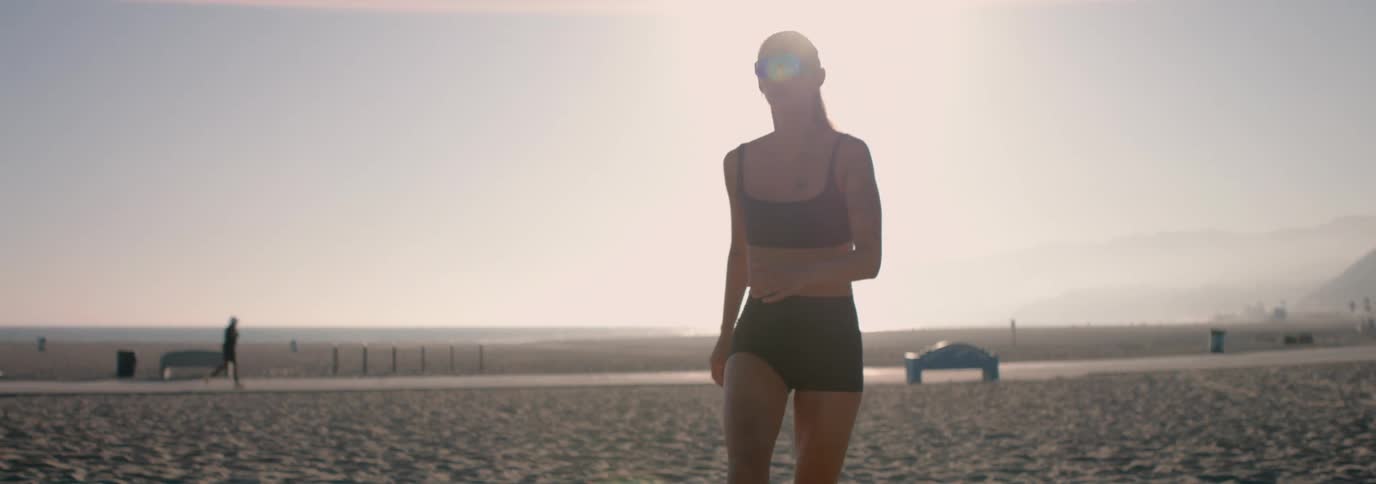 An athletic woman in sunglasses sets a volleyball in the air in slow motion on a hazy beach