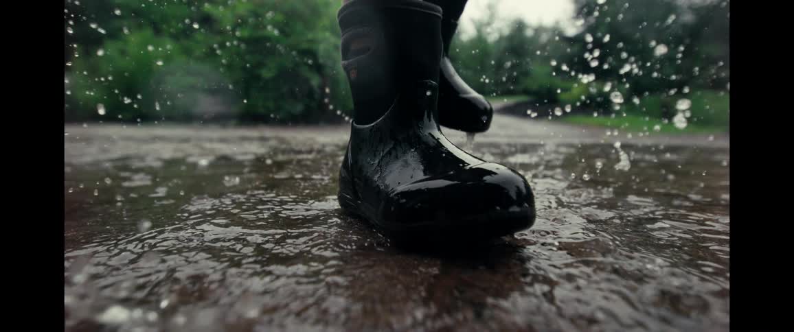 Close up of a black rain boot splashing into a puddle in dramatic super slow motion on a rainy day
