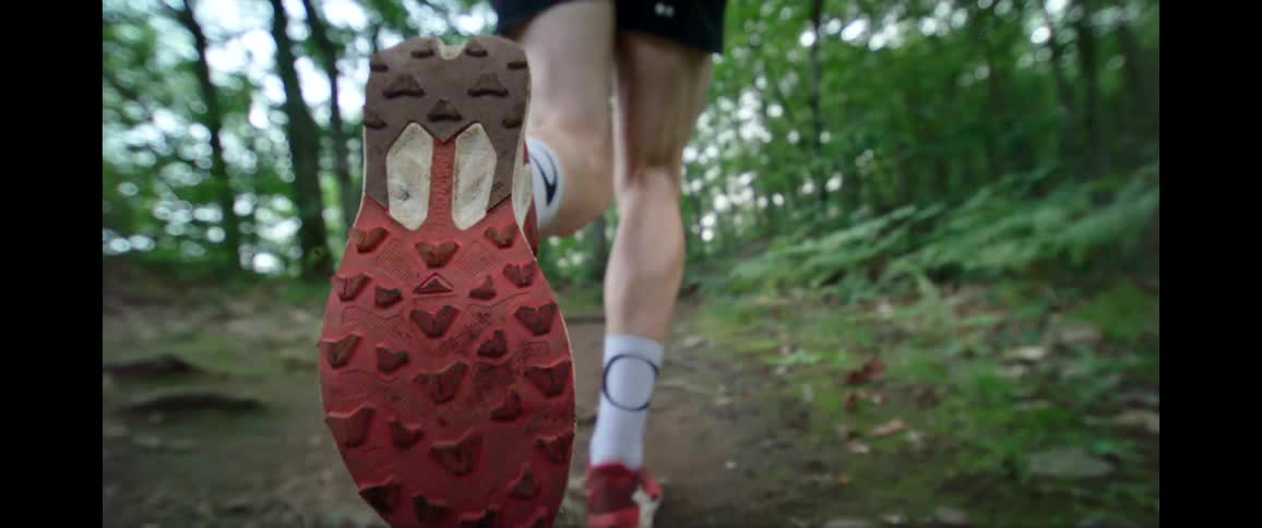Super slow motion close-up of a trail runner's feet and legs moving through a lush green forest
