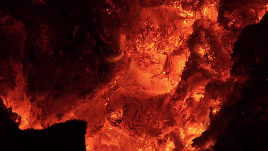 Hot coals smolder and glow with intense heat as small flames dance across the surface