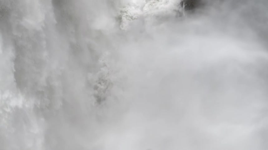 Raging whitewater from a massive waterfall plummets down a dark rock face in extreme slow motion