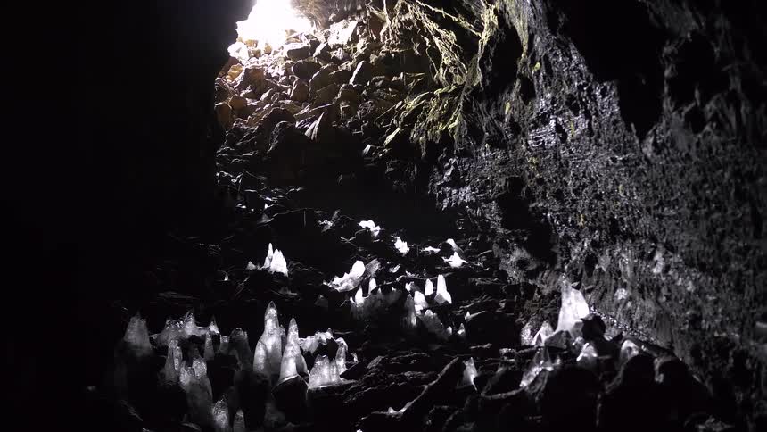 A slow tilt up inside a dark, frozen volcanic cave reveals ice stalagmites growing from the rocky floor