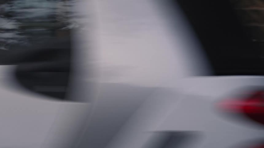 Side-view tracking shot follows the legs of a person running on a city sidewalk, with cars and buildings blurring past
