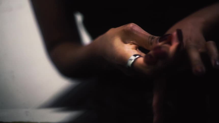Close up shot of a woman's anxious hands as she nervously fidgets with her ring in a dark, moody room