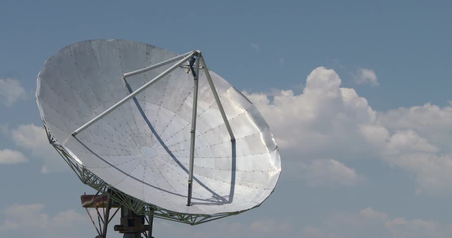A large satellite dish stands still against a blue sky with passing clouds