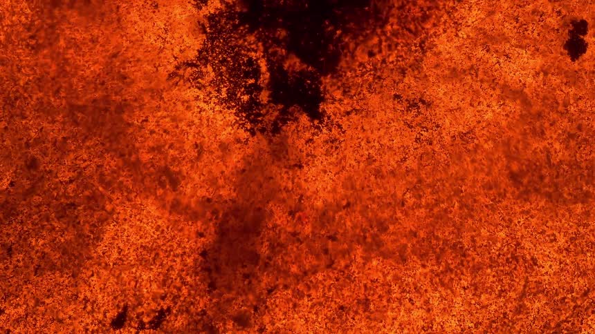 A macro, top-down view of fiery orange and black particles slowly reacting and expanding