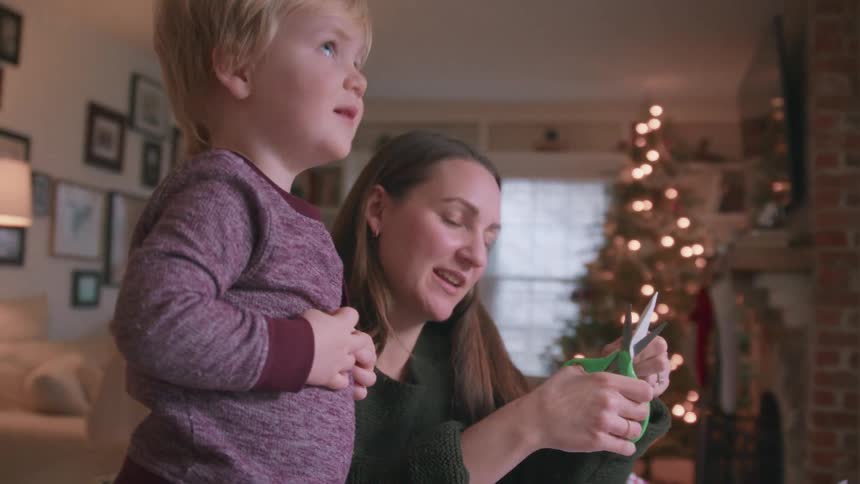 A mother and her toddler son make Christmas crafts together in their festively decorated living room