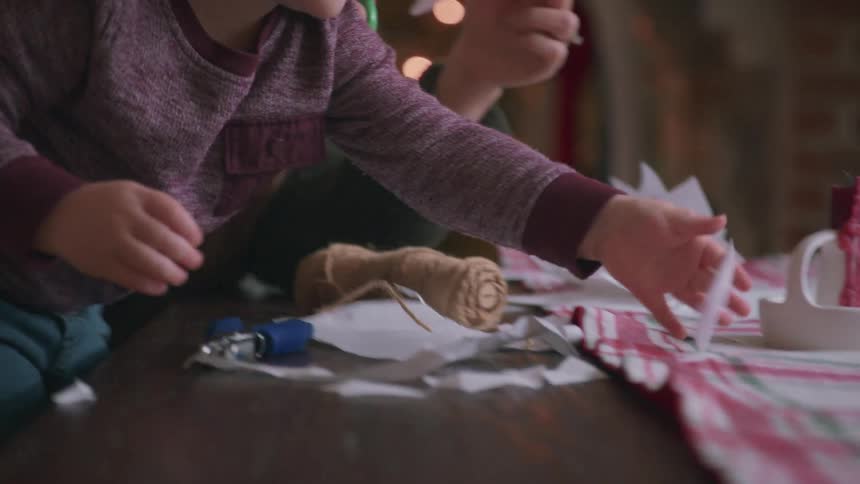 A mother and her young son share a festive moment making paper snowflakes together in their cozy home with a Christmas tree in the background