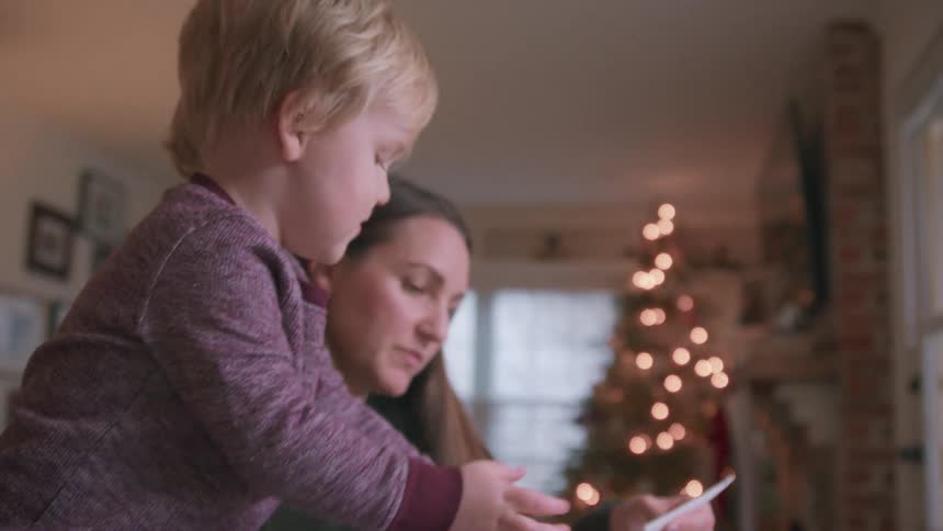 A mother and her young son laugh together while making homemade Christmas decorations with paper and twine