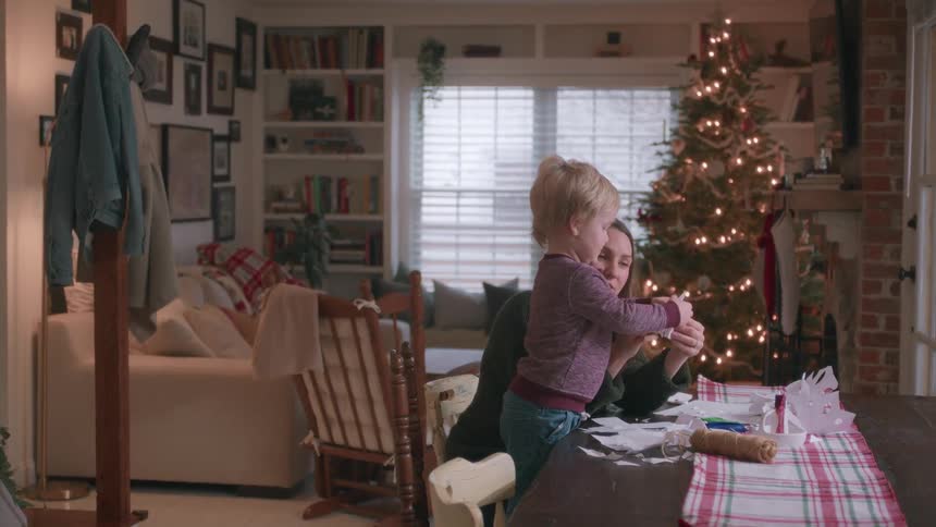 A mother and her toddler son enjoy a festive afternoon making paper snowflakes together in their cozy, Christmas-decorated home
