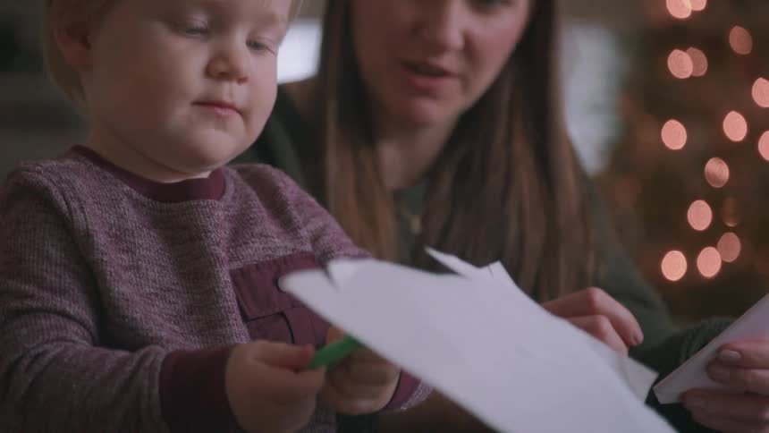 A loving mother patiently teaches her young son how to cut paper with scissors to make Christmas decorations