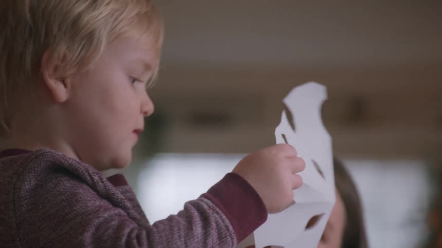 A young boy carefully unfolds a paper snowflake he made with his mother for Christmas in slow motion