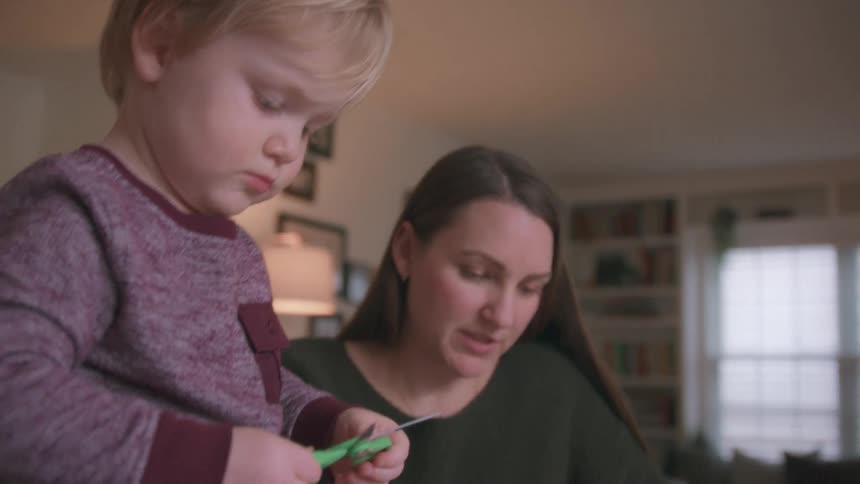A mother and her young son make paper snowflakes together at a table in their cozy home during the holidays