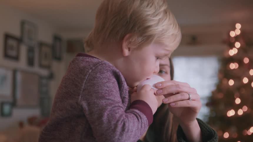 A mother and her young son laugh together while making paper snowflakes for Christmas in their cozy living room