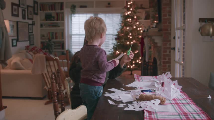 A heartwarming family moment as a mother and her toddler craft paper snowflakes for Christmas and wave to a family member outside
