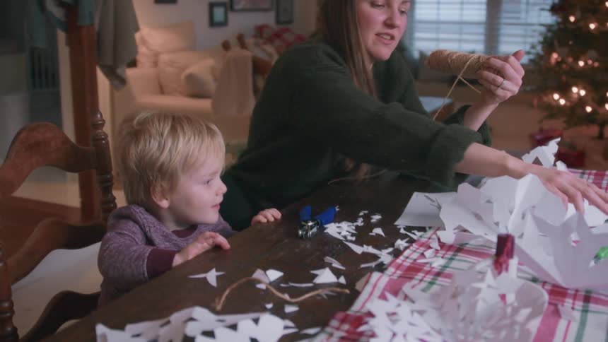 A happy mother and her young son enjoy making paper snowflakes and Christmas decorations together at their dining room table