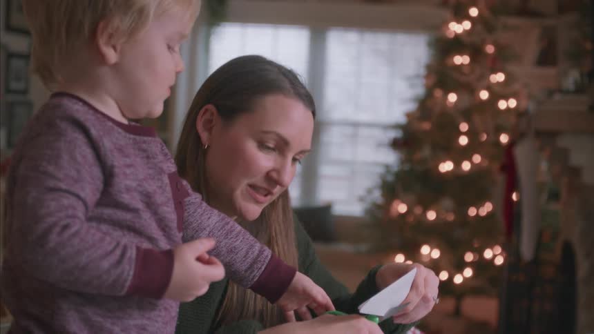 A mother and her young son make Christmas crafts together in front of a twinkling Christmas tree