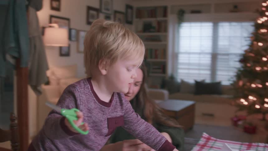 A loving mother and her adorable toddler son make paper snowflakes together for Christmas in their cozy home
