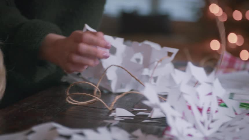 A mother and child work together making a paper snowflake garland for Christmas