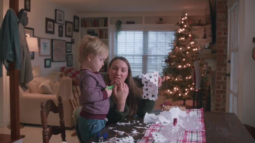 A loving mother shows her toddler son the finished paper snowflake they are making together for Christmas