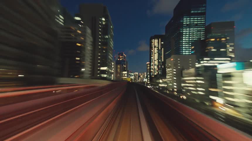 A mesmerizing hyper-lapse captures the view from a high-speed train as it speeds through a dazzling, futuristic cityscape at night