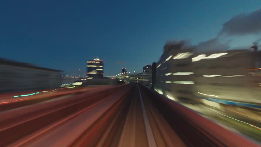 A futuristic point-of-view time-lapse of a train speeding through the brightly lit city of Tokyo at night