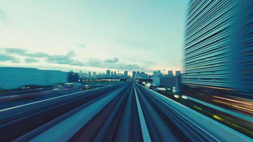 Point-of-view timelapse of a high-speed train ride through a teal-toned futuristic cityscape at dusk