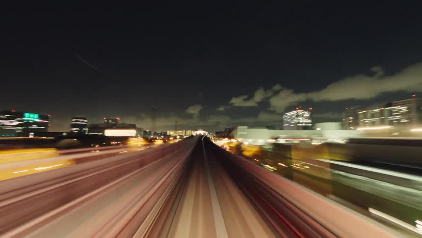 Point-of-view time-lapse of a high-speed monorail journey through a modern city's illuminated landscape at night