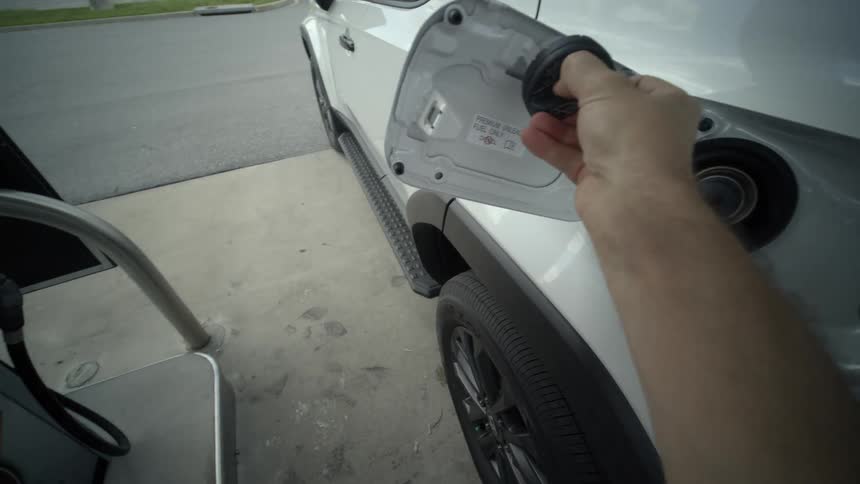 A first-person point of view of a person opening the gas cap on a white truck and preparing to pay at the pump