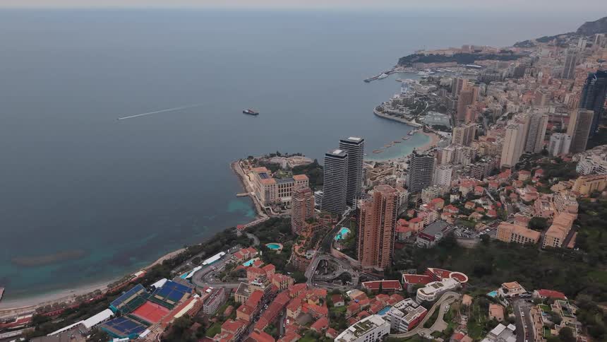 A static aerial view shows the dense cityscape of Monaco overlooking the Mediterranean Sea on a cloudy day