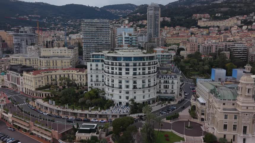 An aerial view slowly pushes in on the iconic Casino de Monte-Carlo and surrounding luxury hotels and apartments in Monaco on a cloudy day