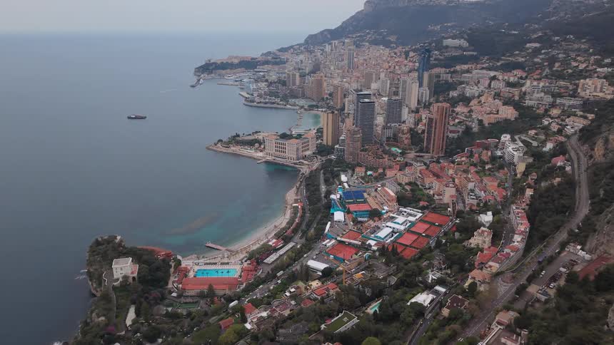 A stunning aerial view reveals the city of Monaco nestled between the mountains and the sea on an overcast day